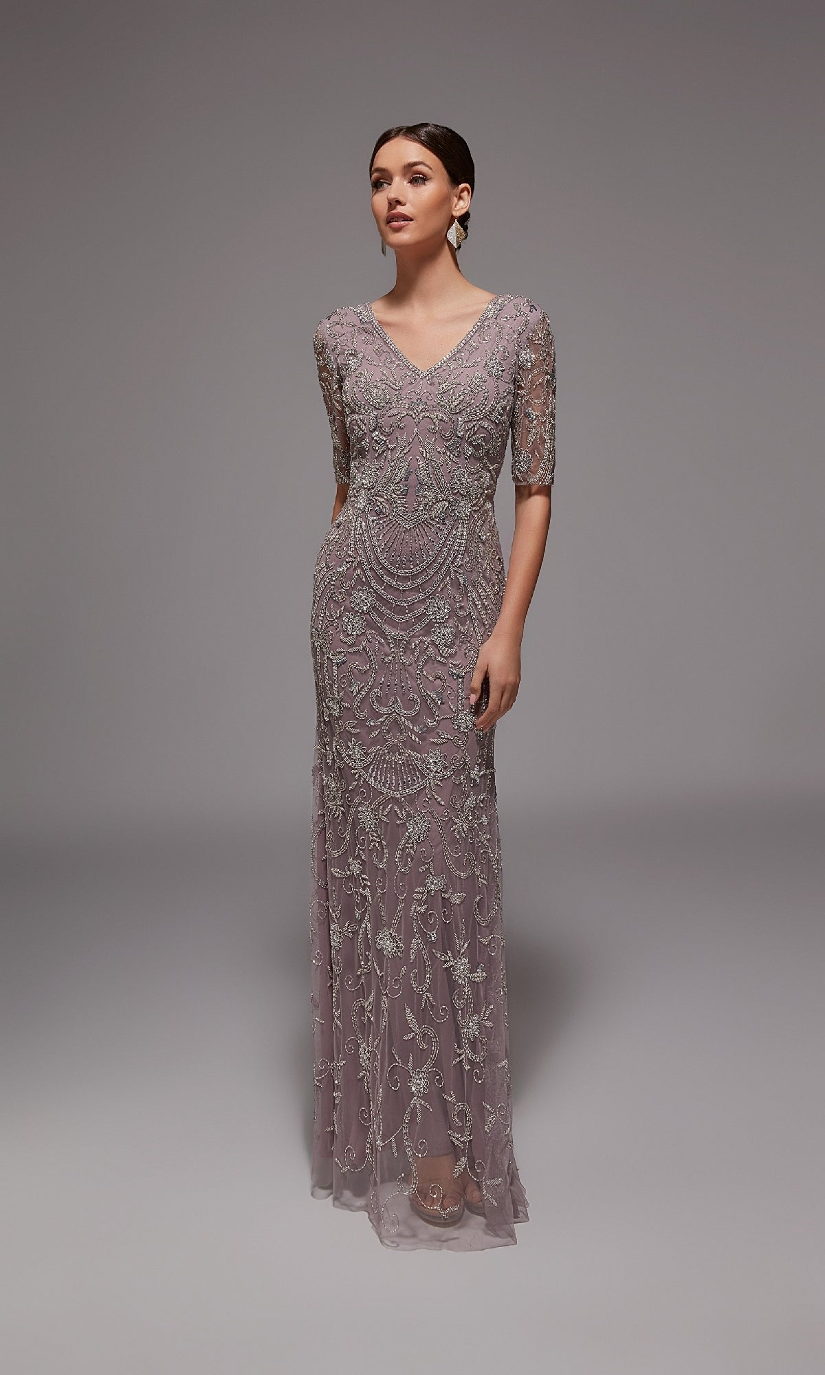 A woman wears the Alyce 27824 long formal dress in Lilac Grey/Silver, featuring beaded embroidery and elegant details, standing against a plain gray background—ideal for formal occasions.